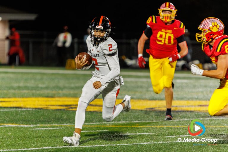 St. Charles East quarterback Cruz Herrera (#2) scrambles upfield while being pursued by Batavia defensive lineman Gavin Pecor (#90) during the DuKane Conference game on Friday, Oct. 17, 2025, in Batavia, Illinois. Batavia defeated St. Charles East 31-13. (Photo Credit: Zachary Gebis)